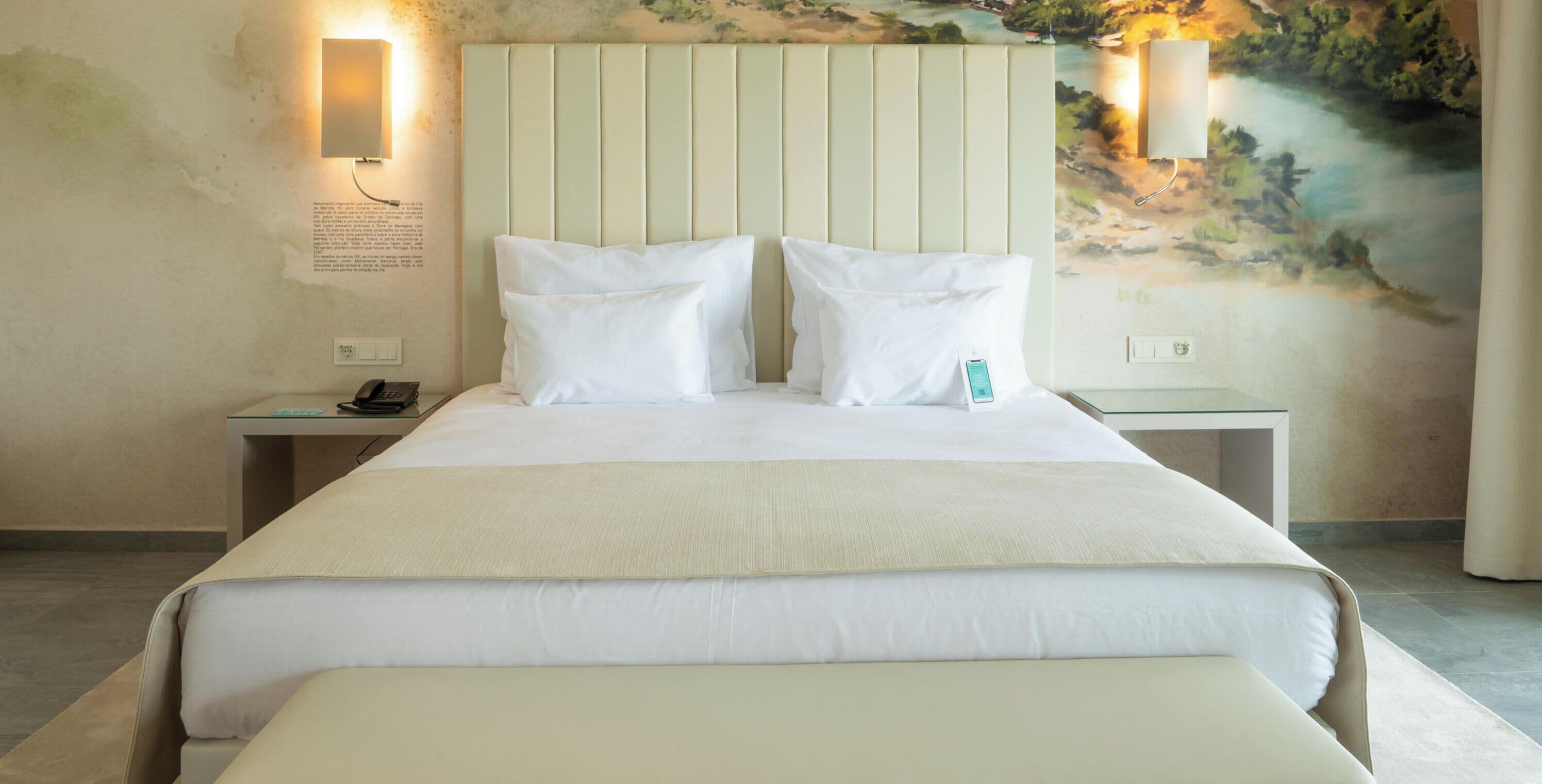 A hotel room with a large bed, two bedside tables, a nightstand, a wall-mounted lamp, and a mural.