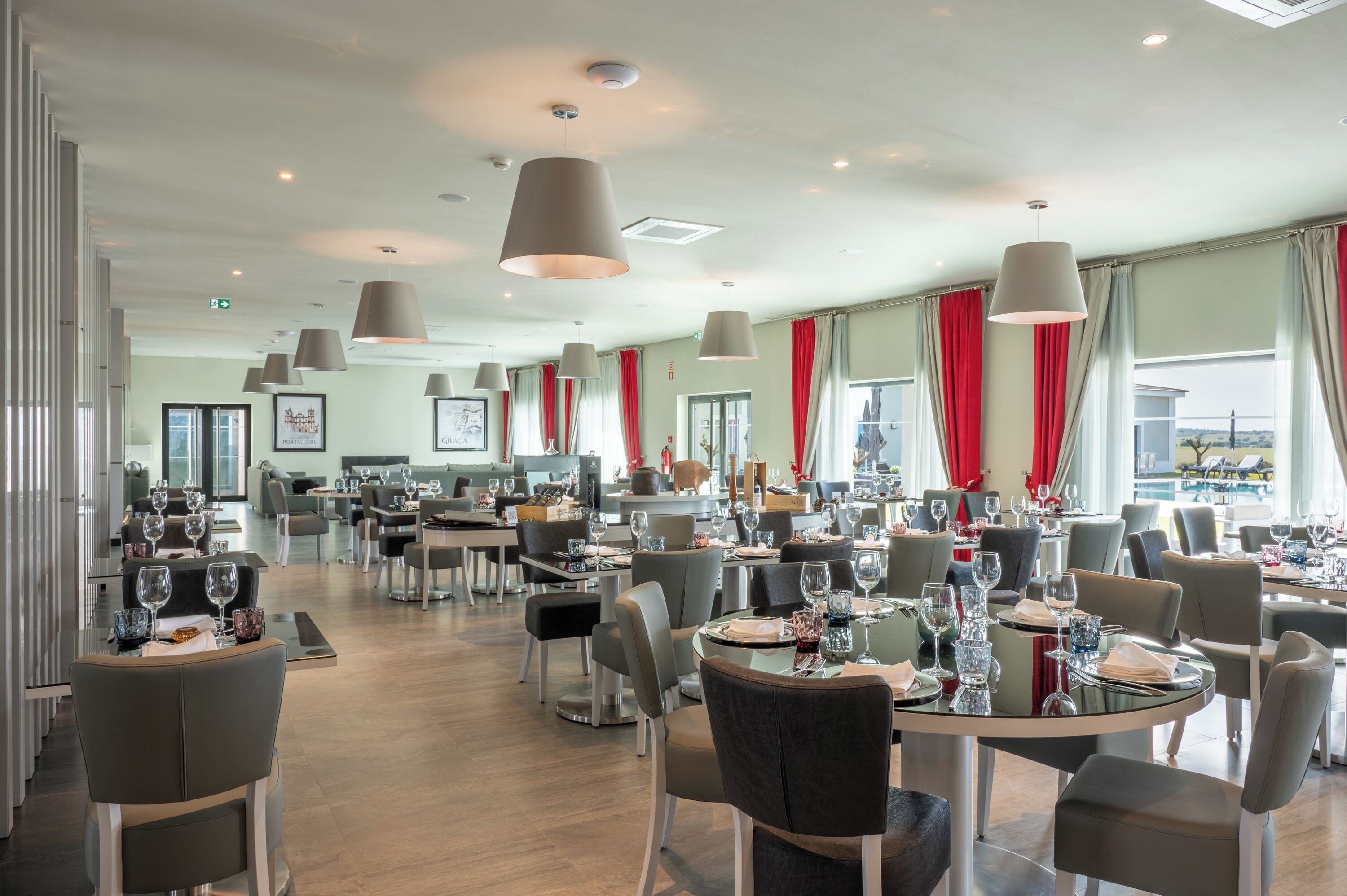 Un restaurante moderno con varias mesas, sillas grises e iluminación colgante.