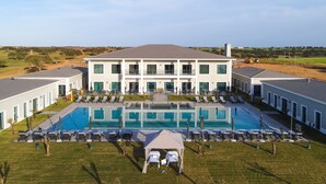 A modern hotel with a large pool, multiple balconies, and a view of the surrounding landscape. - Vila Gale Collection Hotel Monte do Vilar (Beja)