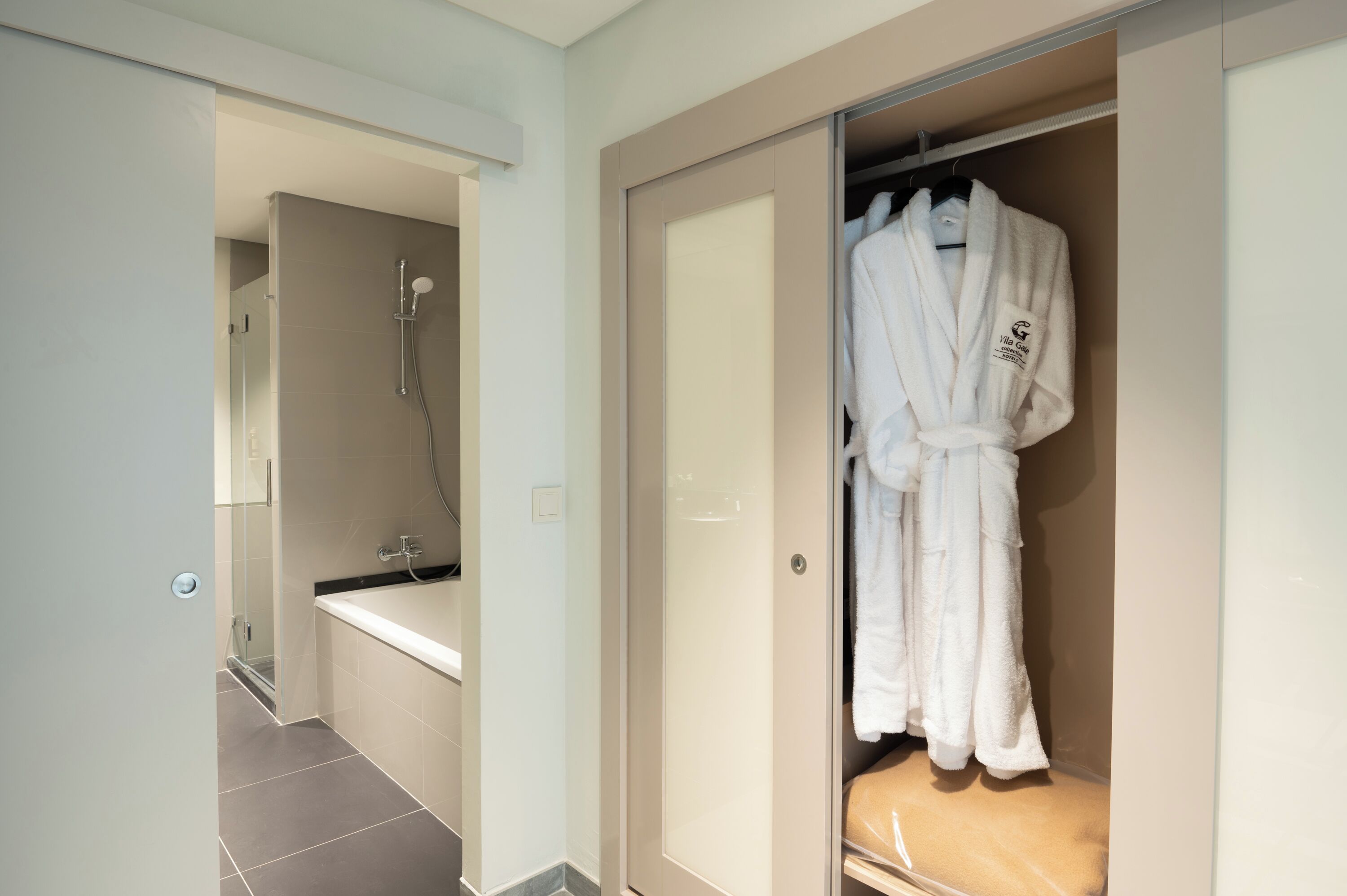 A modern bathroom with a shower, a bathtub, and a walk-in closet with a robe hanging.