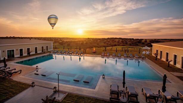 A swimming pool with lounge chairs and a hot air balloon in the sky. - Vila Gale Collection Hotel Monte do Vilar (Beja)