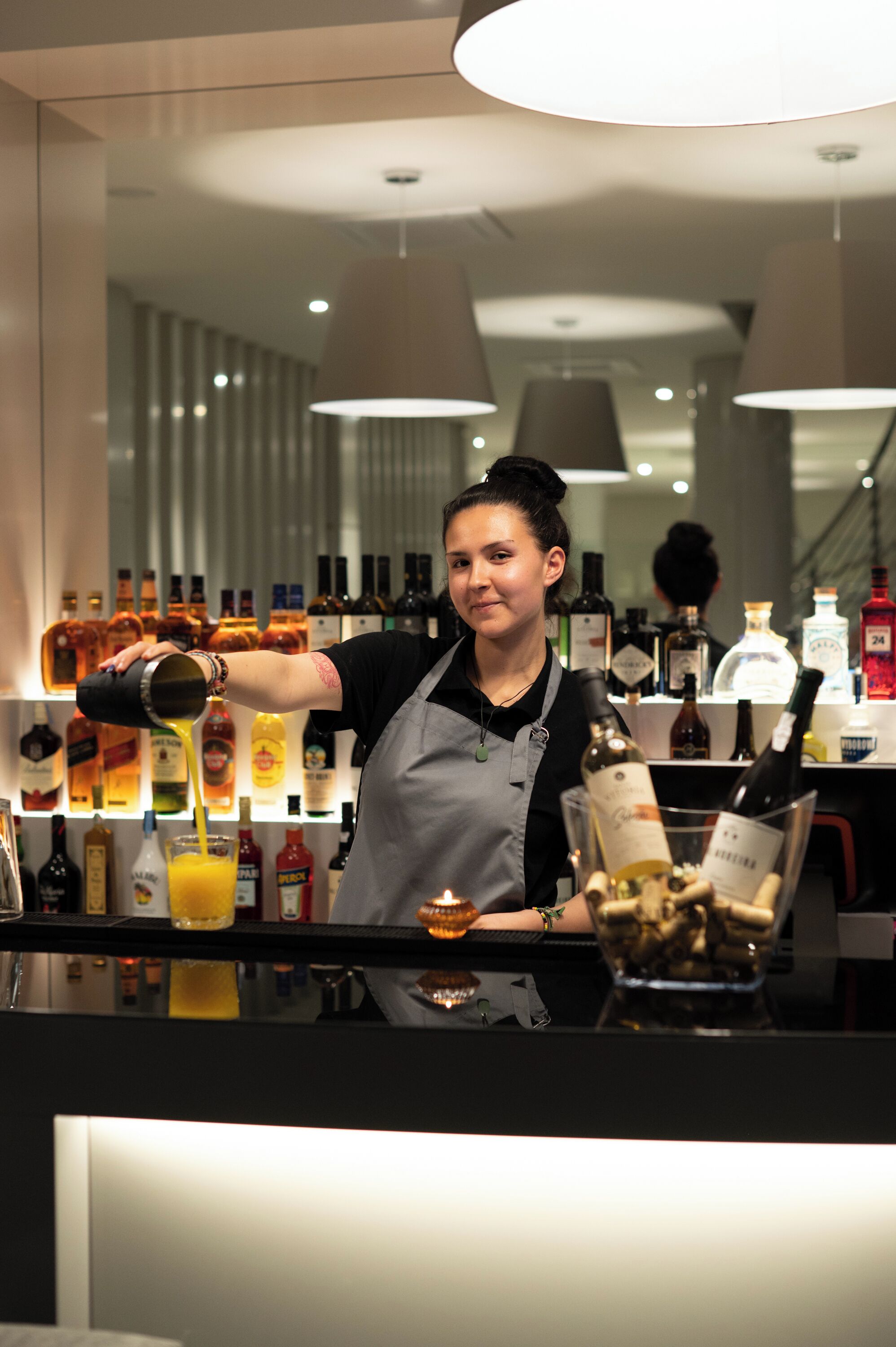 A bar area with a bartender pouring a drink, bottles of alcohol, and a wine glass on the counter.
