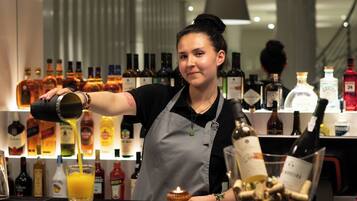 A bar area with a bartender pouring a drink, bottles of alcohol, and a wine glass on the counter.