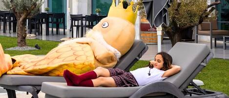 Un niño recostado en una tumbona al lado de una gran estatua de mascota.