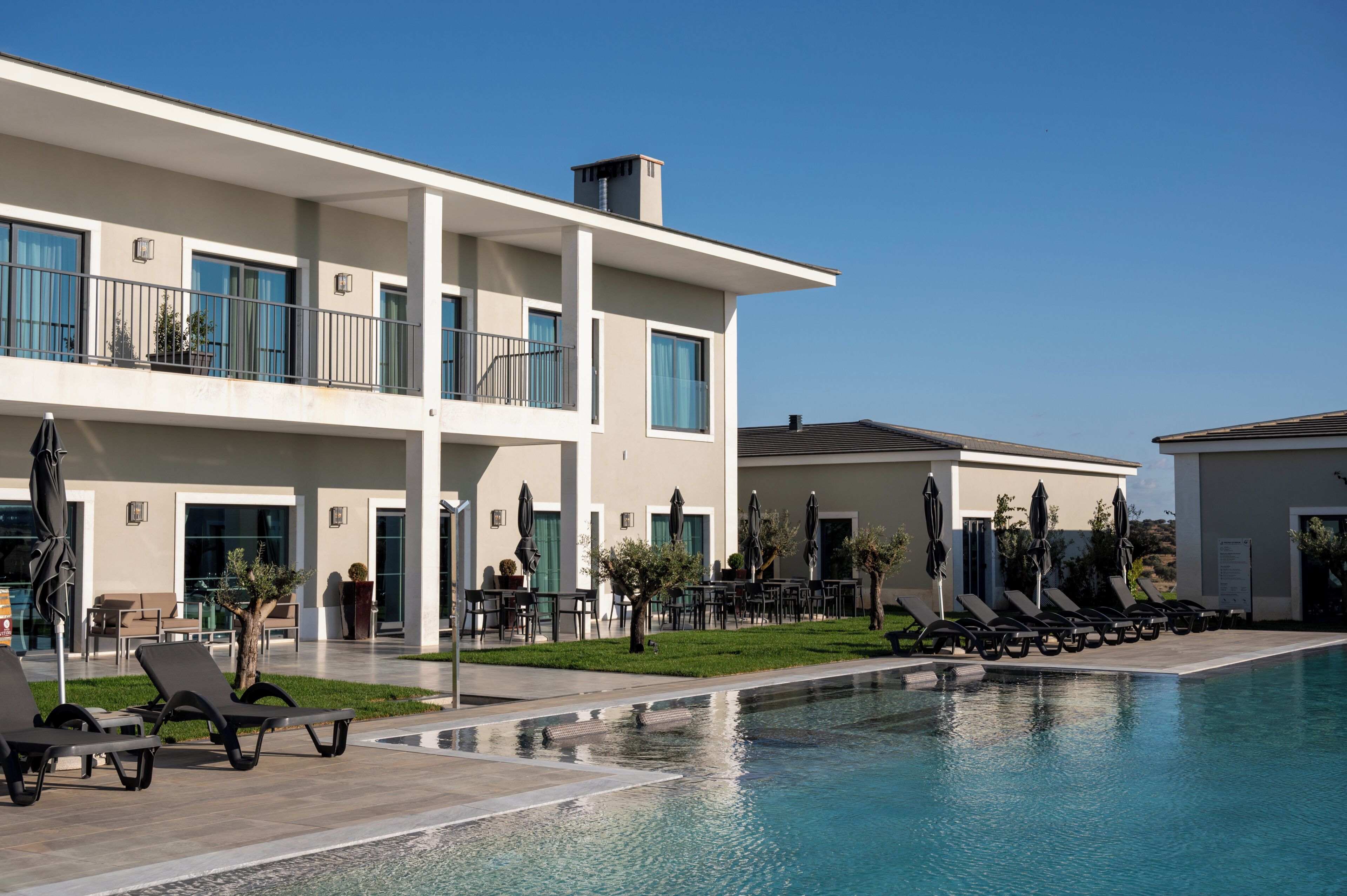 A modern hotel with a pool, outdoor seating, and a clear blue sky.