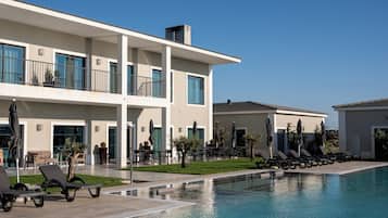A modern hotel with a pool, outdoor seating, and a clear blue sky.