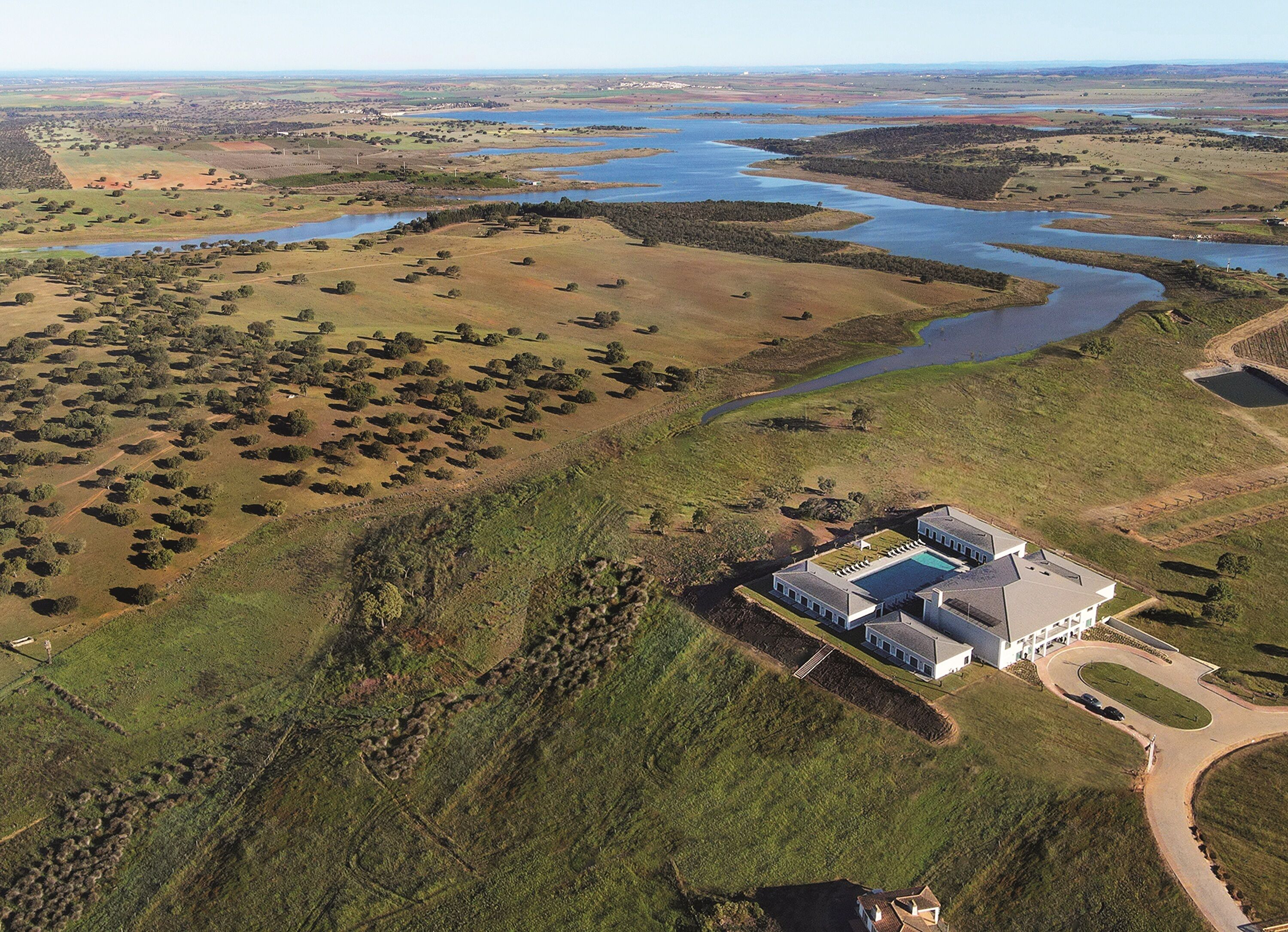 An aerial view of a large estate with a swimming pool, surrounded by expansive fields and a river.