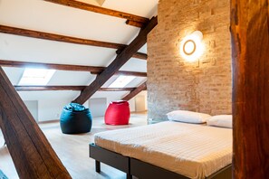 A loft bedroom with exposed wooden beams, a brick wall, and a bed with white bedding. - Sacrati 39 | Tourist Apartment in the Historic Center (Ferrara)