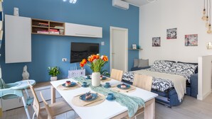 A modern room with a blue accent wall, a flat-screen TV, a dining table set with plates, cups, and a vase of flowers. - OurJoy Condo, 55sm, free private parking and breakfast, high-speed WIFi and A/C (Milano)