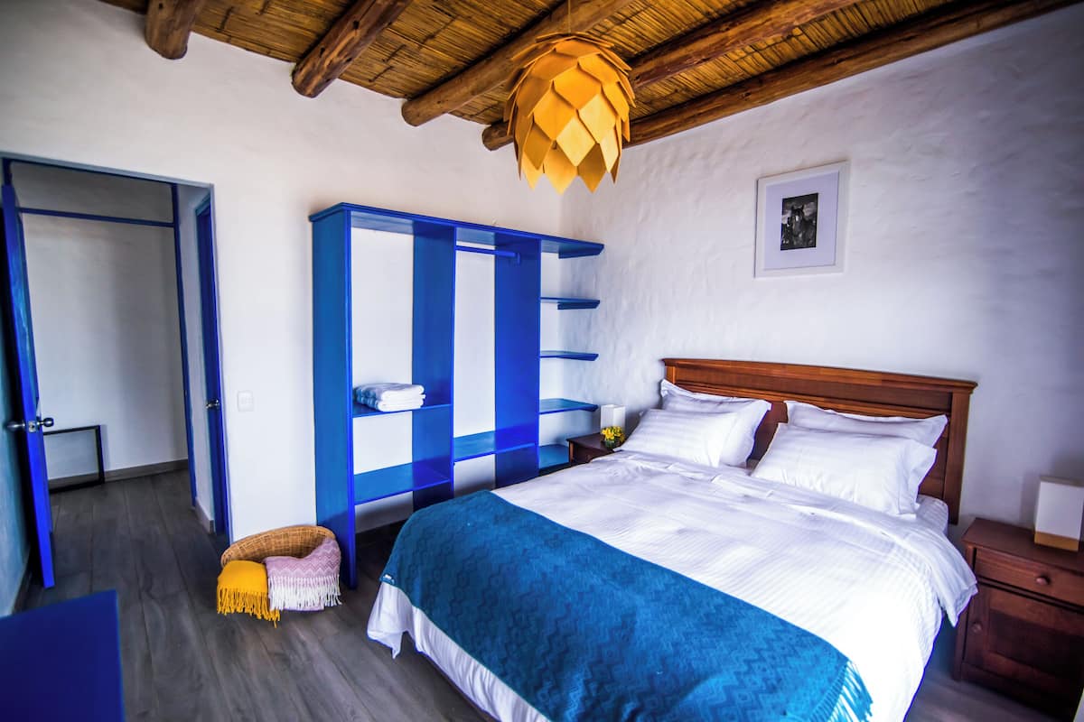 A bedroom with a wooden ceiling, a bed with white bedding, a blue wardrobe, and a small nightstand.