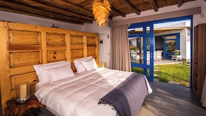 A bedroom with a wooden headboard, a large bed with white linens, a bedside table with a candle, and a view of an outdoor patio with blue doors.