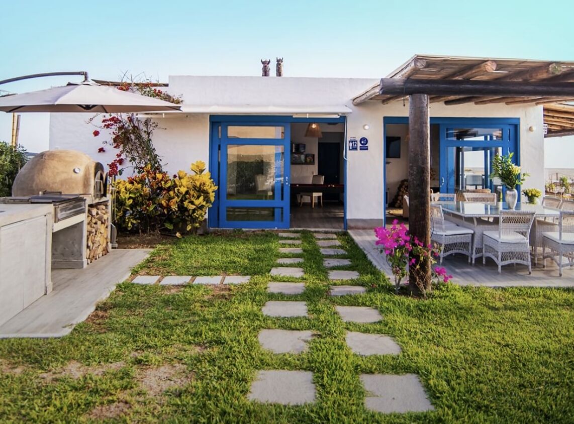 Una casa moderna con puerta azul, zona de barbacoa y jardín con piedras para caminar.