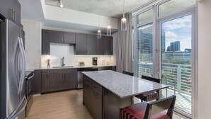Une cuisine moderne avec des meubles de couleur sombre, un plan de travail en granit et une grande fenêtre donnant sur la ville.