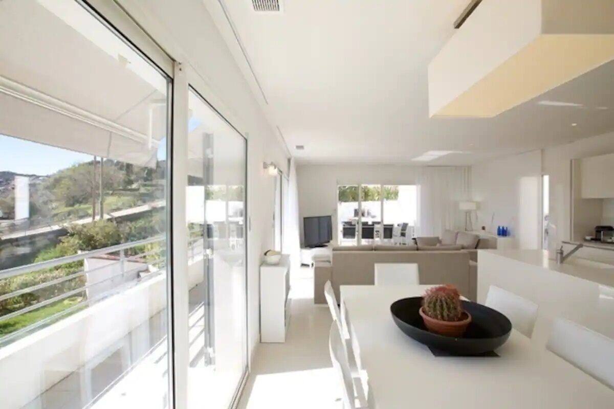 Un interior moderno con zona de comedor, cocina y un amplio ventanal con vistas a la vegetación.