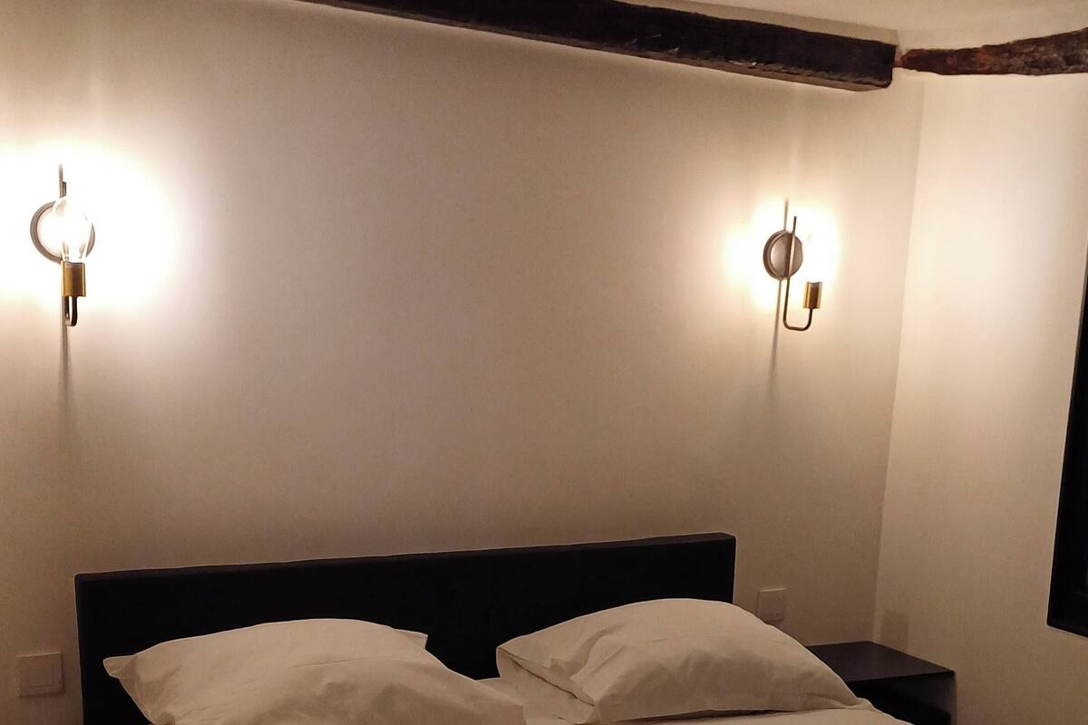 Una cama con ropa de cama blanca, dos lámparas fijadas a la pared y un cabecero oscuro.