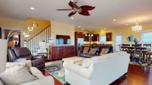 A spacious living room with a white sofa, brown leather chairs, and a patterned rug. A staircase with a wooden railing leads to an upper level. - OCEAN VIBES ON THE INTRACOASTAL (Wilmington)