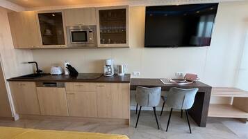 Una cocina moderna con microondas, estufa y pileta, un televisor de pantalla plana montado en la pared y un comedor con dos sillas.