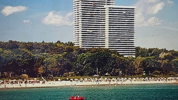Un hotel alto y moderno con techo plano y líneas horizontales, cerca de una playa bajo un cielo azul despejado.
