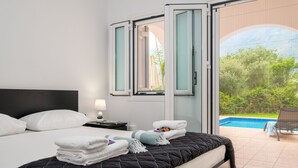 A hotel room with a bed, a nightstand, a lamp, a window with a view of a swimming pool and greenery. - Kournas-sleeps8-parking-garden-pool-petfriendly (Apokoronas)