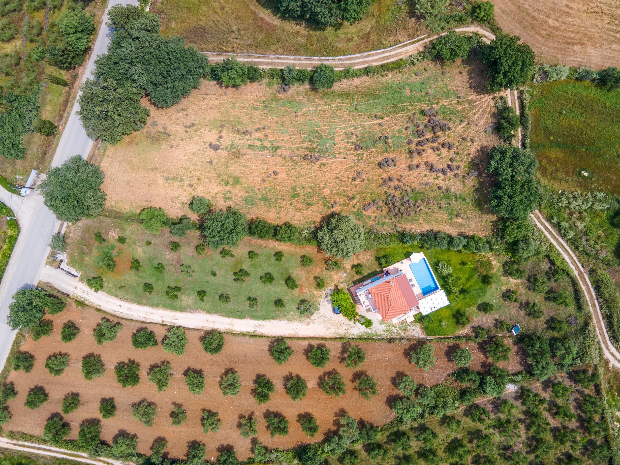 An aerial view of a property with a swimming pool, a large open field, and a road curving through the landscape.