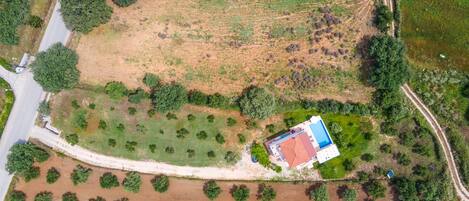 An aerial view of a property with a swimming pool, a large open field, and a road curving through the landscape.