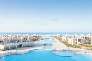 A resort with multiple swimming pools, a bridge, and a view of the sea. - Gewan Resort New Alamein (Marsa Matrouh)