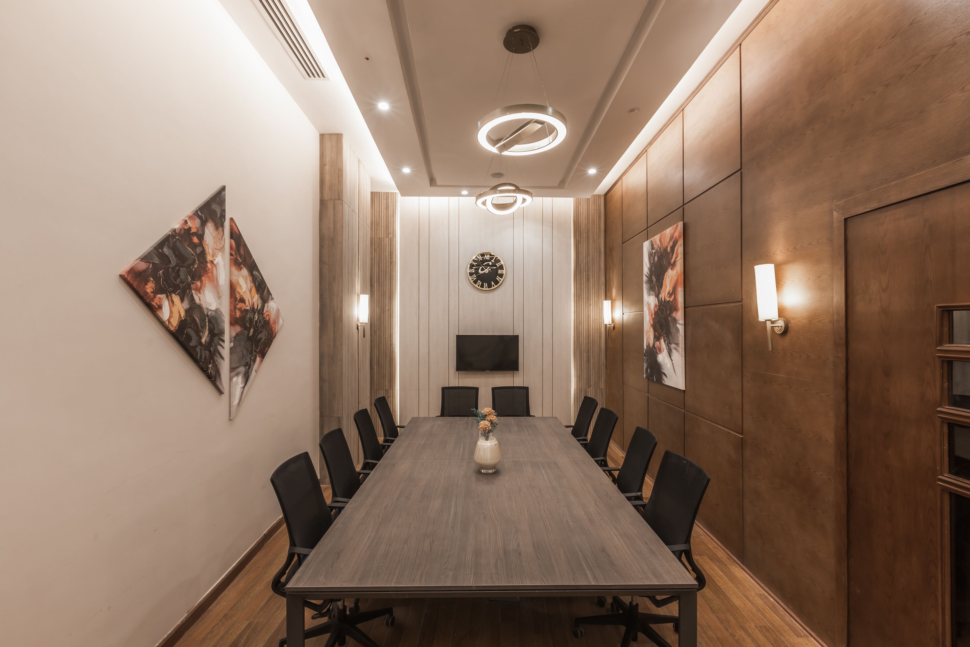 Una sala de conferències amb una taula llarga, cadires, un rellotge i obres d'art a les parets.