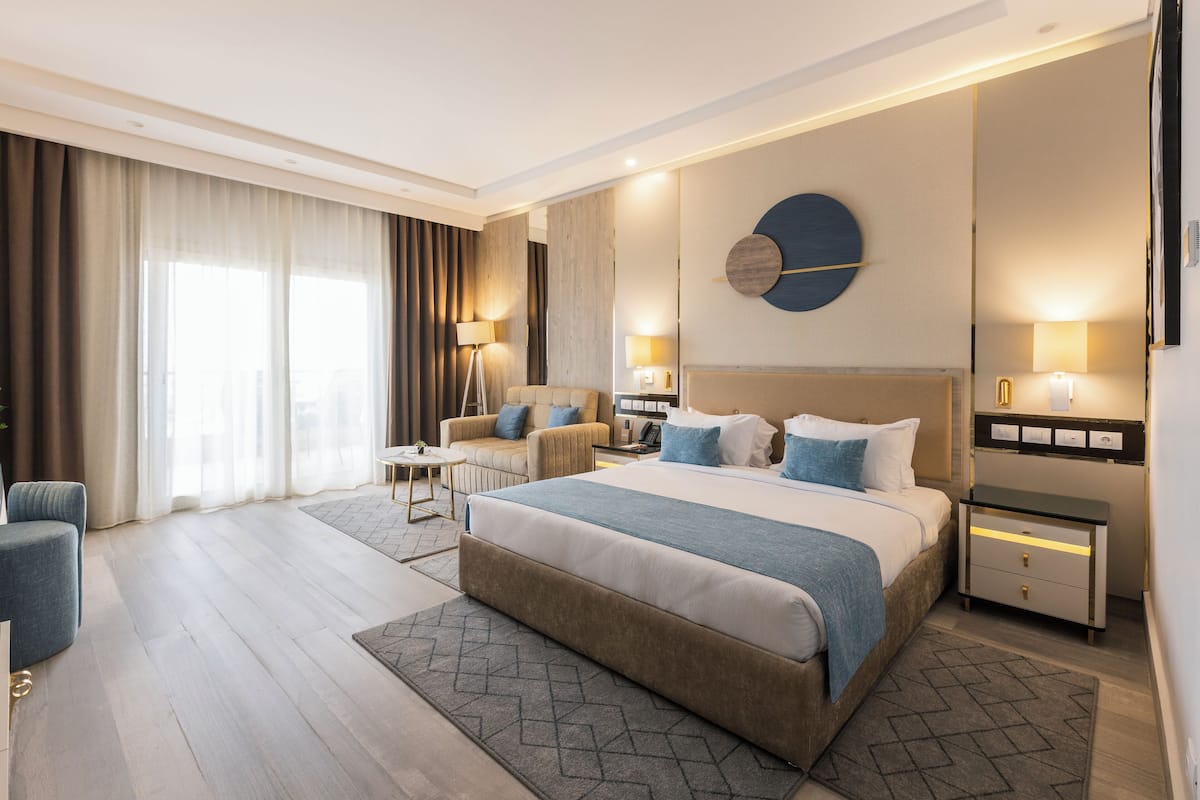 A modern hotel room with a large bed, a sofa, a desk, and a lamp.