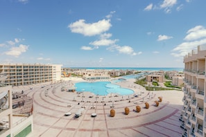 Um resort com piscina central, vários edifícios e céu claro.