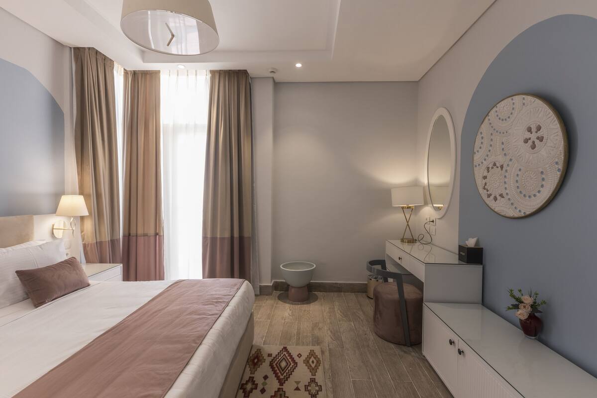 A modern hotel room with a large bed, a bedside table, a mirror, a dresser, and a small round table.