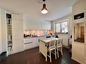 A modern kitchen with white cabinets, a dining table with chairs, and a pendant light. - Great 1 Bedroom Flat in Solna (Solna)