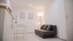 Una sala de estar moderna con un sofá gris, una mesa blanca con dos sillas y dos cuadros en la pared.