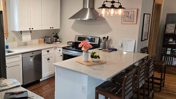 A modern kitchen with white cabinets, a stainless steel range hood, a central island with bar stools, and a pendant light fixture. - Located in beautiful/historic downtown Peninsula in the heart of a National Park (Peninsula)