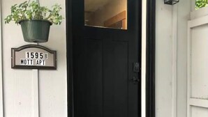 A black door with a small window, a hanging planter with green plants, and a doormat on a wooden porch. - Located in beautiful/historic downtown Peninsula in the heart of a National Park (Peninsula)