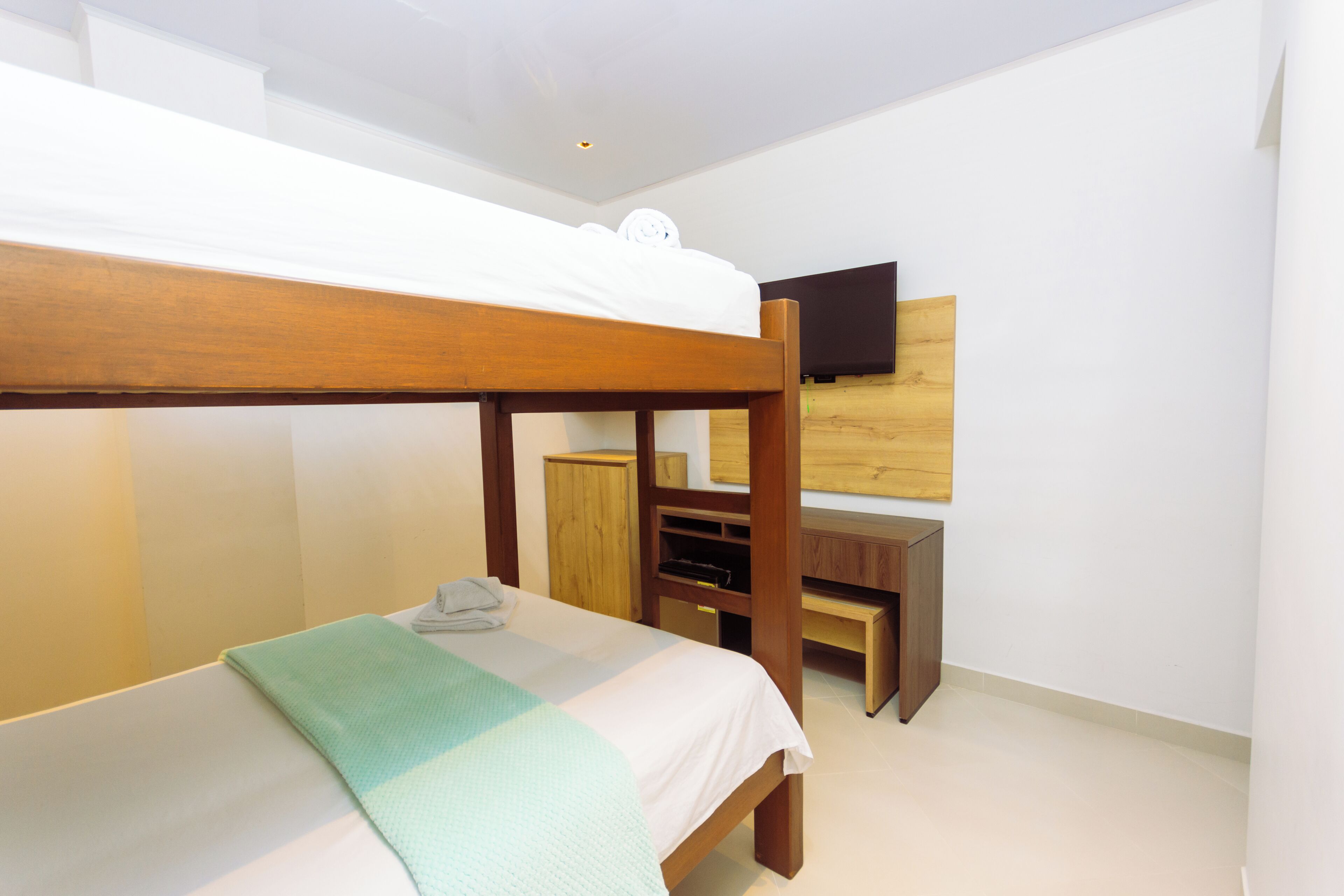 A bunk bed with a wooden frame, a desk, and a television mounted on the wall.