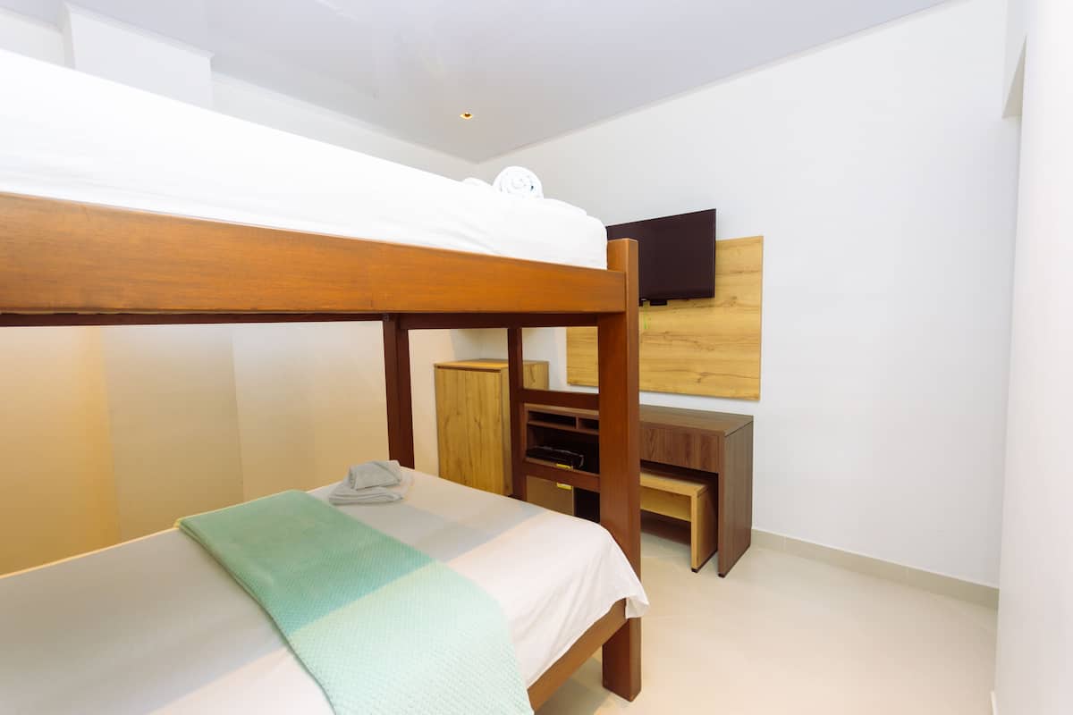 A bunk bed with a wooden frame, a desk, and a television mounted on the wall.