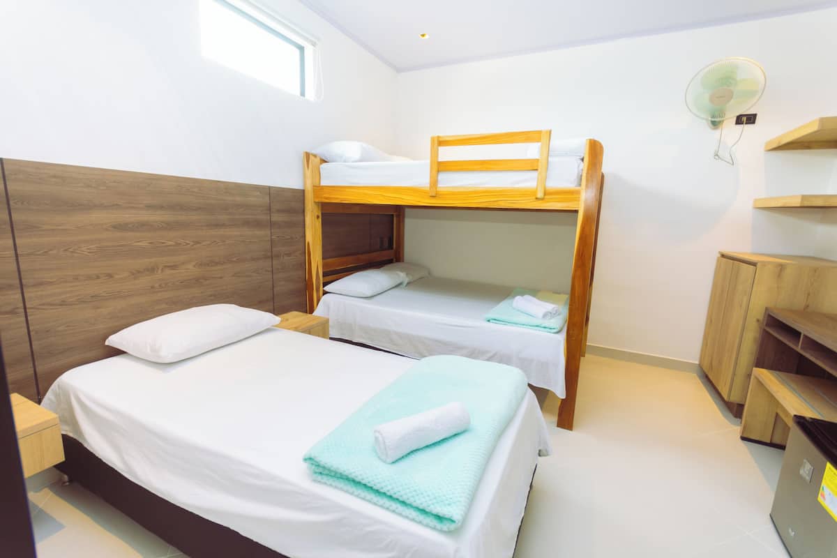 A bunk bed room with a wooden headboard, a bedside table, a fan, and a small wooden cabinet.