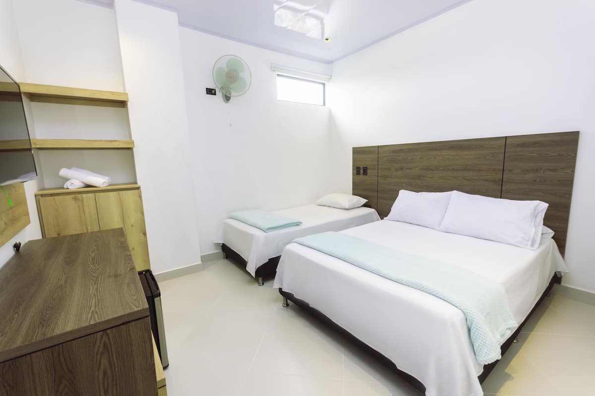 A bedroom with two beds, a wooden desk, a fan, and a window.