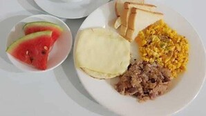 A table with a meal consisting of soup, toast, scrambled eggs, and a fruit salad.