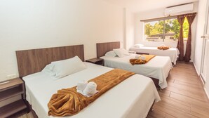 A hotel room with three beds, a window with curtains, and an air conditioning unit.