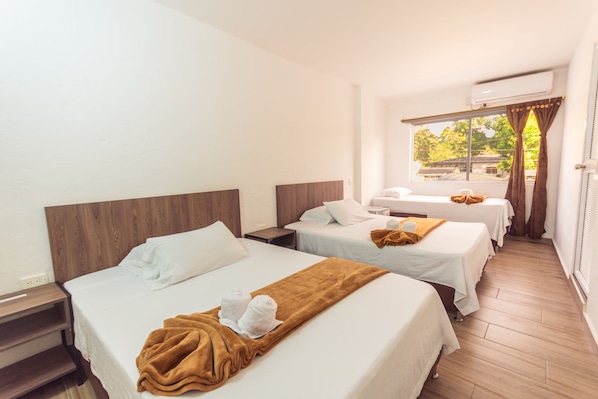 A hotel room with two beds, a window with curtains, and an air conditioning unit.