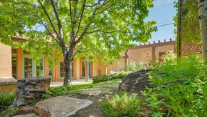 A courtyard with a tree, rock formations, and a building with orange walls and green doors. - Luxe & Stylish Santa Fe Home Rental Near Downtown! (Santa Fe)