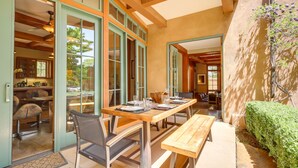 An open-plan dining area with a wooden table and chairs, a bench, and a view of the kitchen through glass doors. - Luxe & Stylish Santa Fe Home Rental Near Downtown! (Santa Fe)