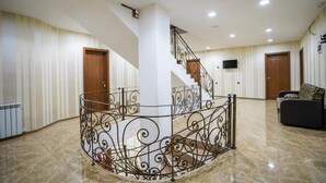 A spacious interior with a central spiral staircase, a flat-screen TV mounted on the wall, and a patterned sofa in the corner. - Natali Hotel (Borjomi)