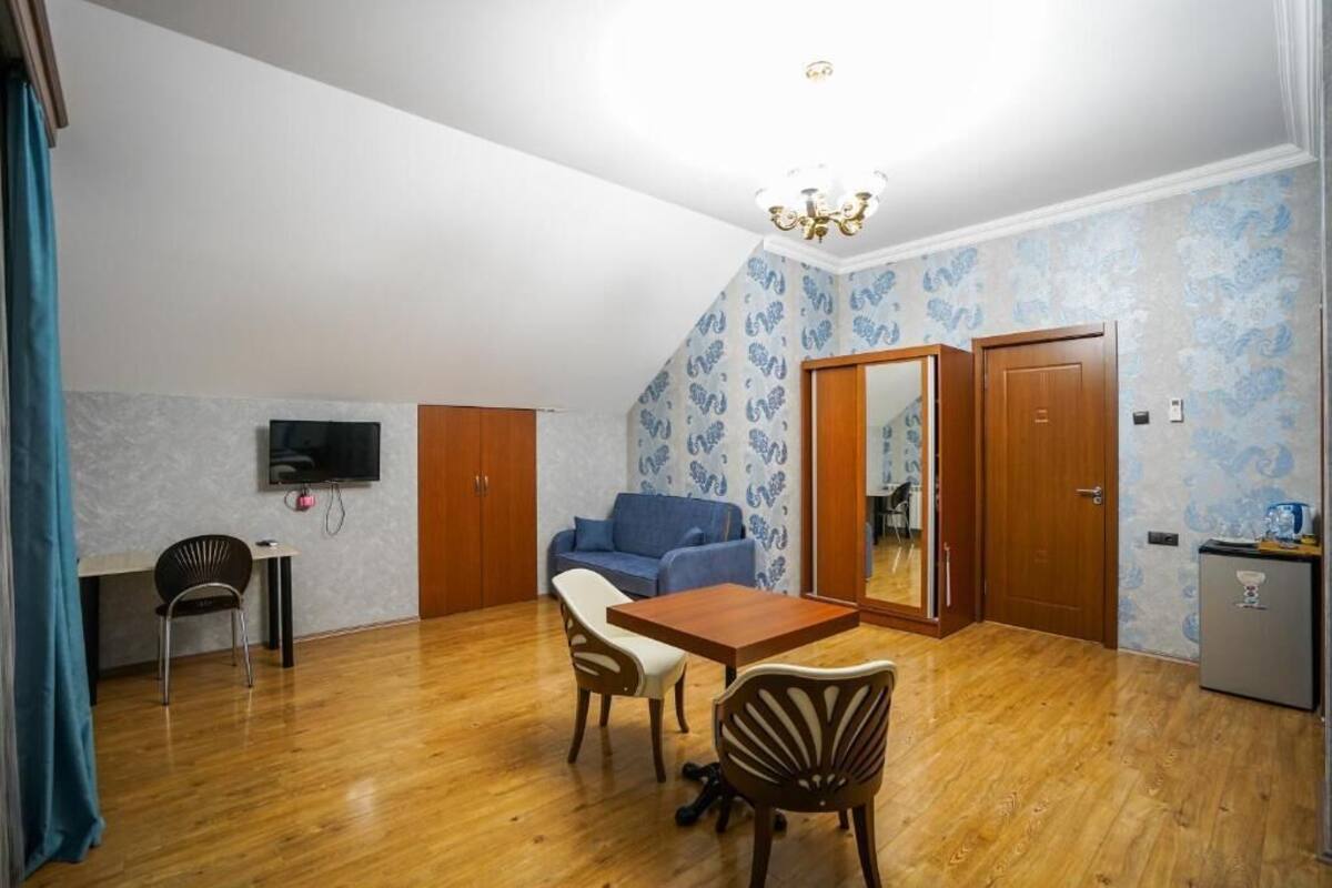 A compact living space with a dining area, a sofa, a TV mounted on the wall, and a small kitchenette.