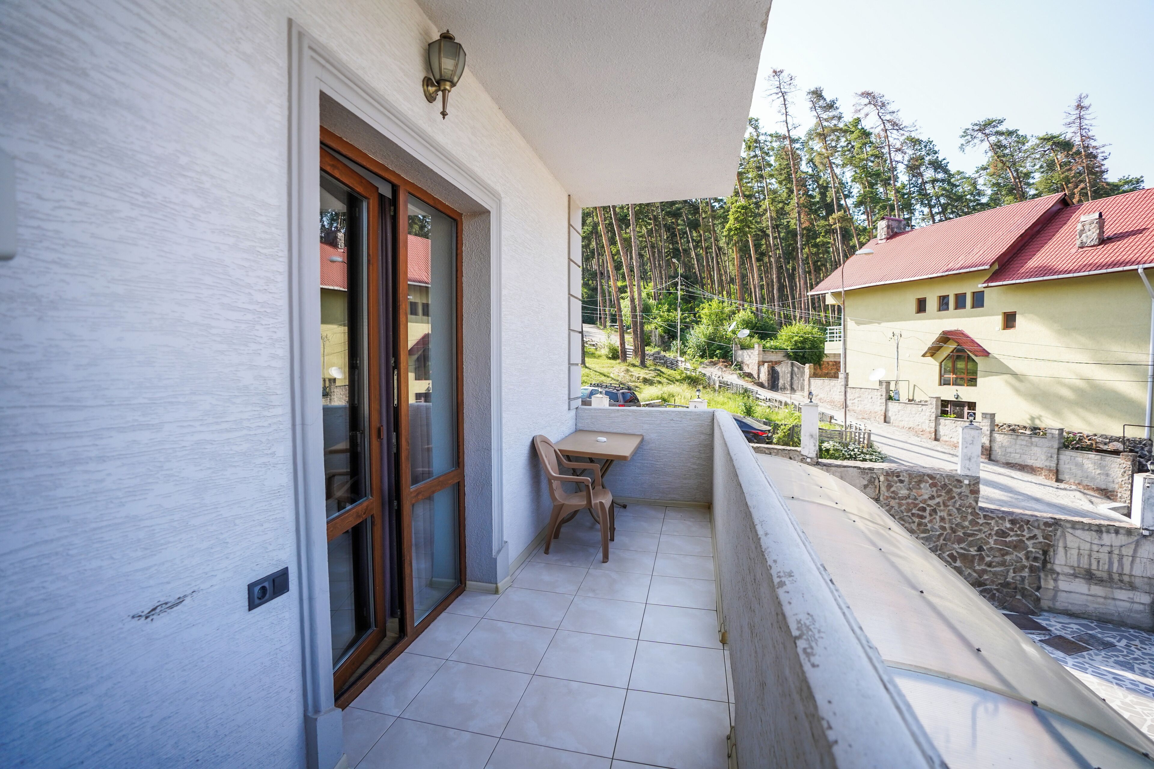 Un balcone con tavolo e sedia, una porta e vista su una zona boschiva.