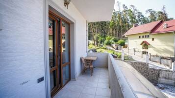 Un balcone con tavolo e sedia, una porta e vista su una zona boschiva.