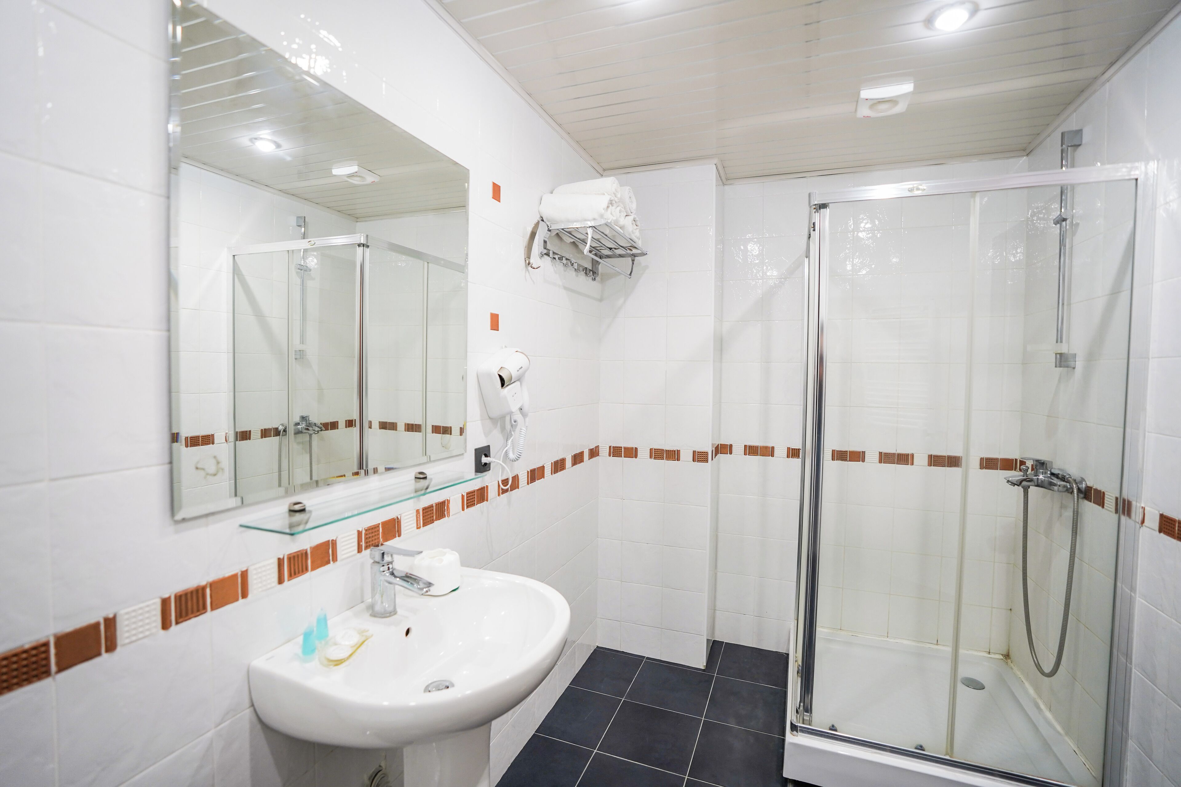 Un baño moderno con cabina de ducha de vidrio, un lavabo blanco con espejo arriba y un perchero con una toalla.