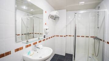 Un baño moderno con cabina de ducha de vidrio, un lavabo blanco con espejo arriba y un perchero con una toalla.
