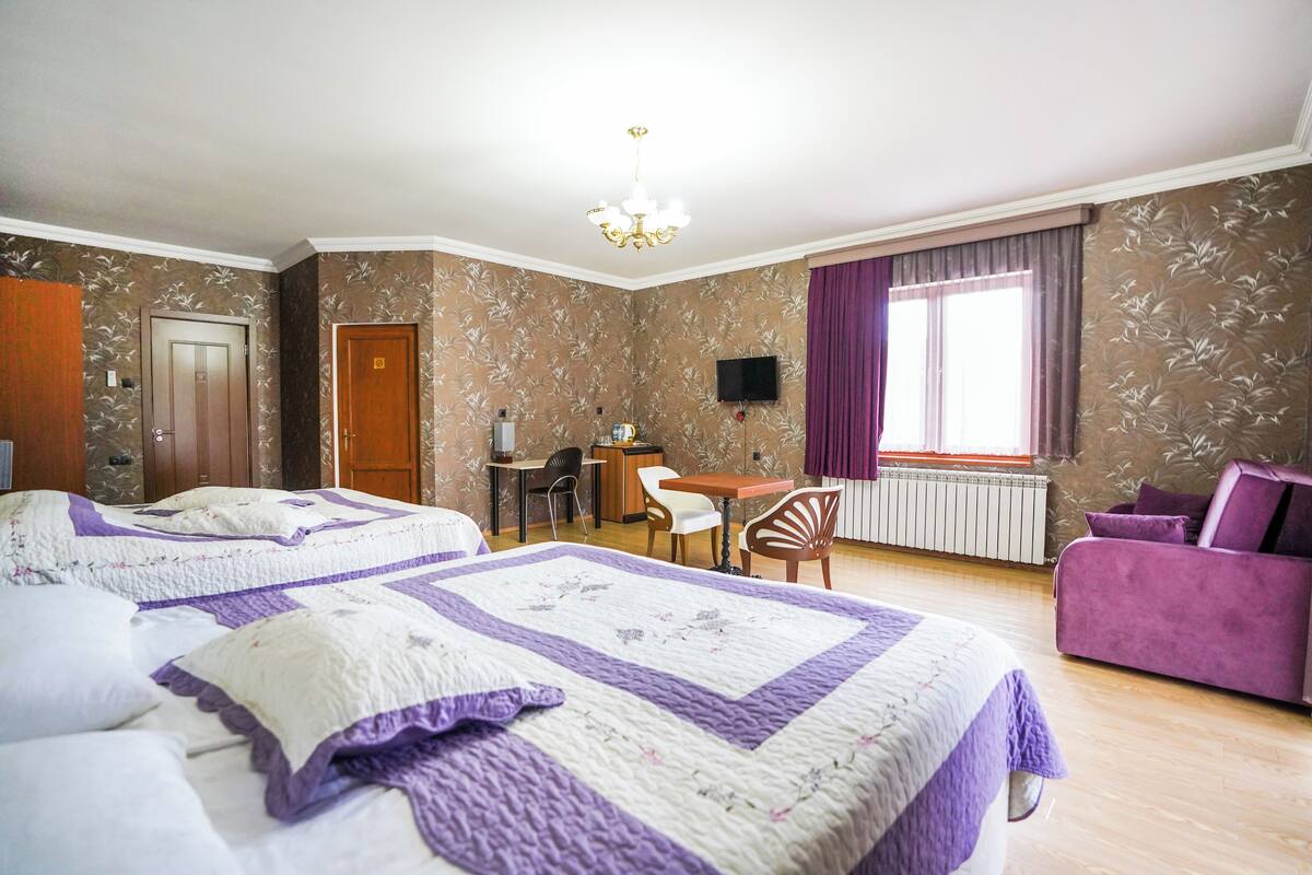 A hotel room with two beds, a desk, a chair, a TV, and a purple sofa.